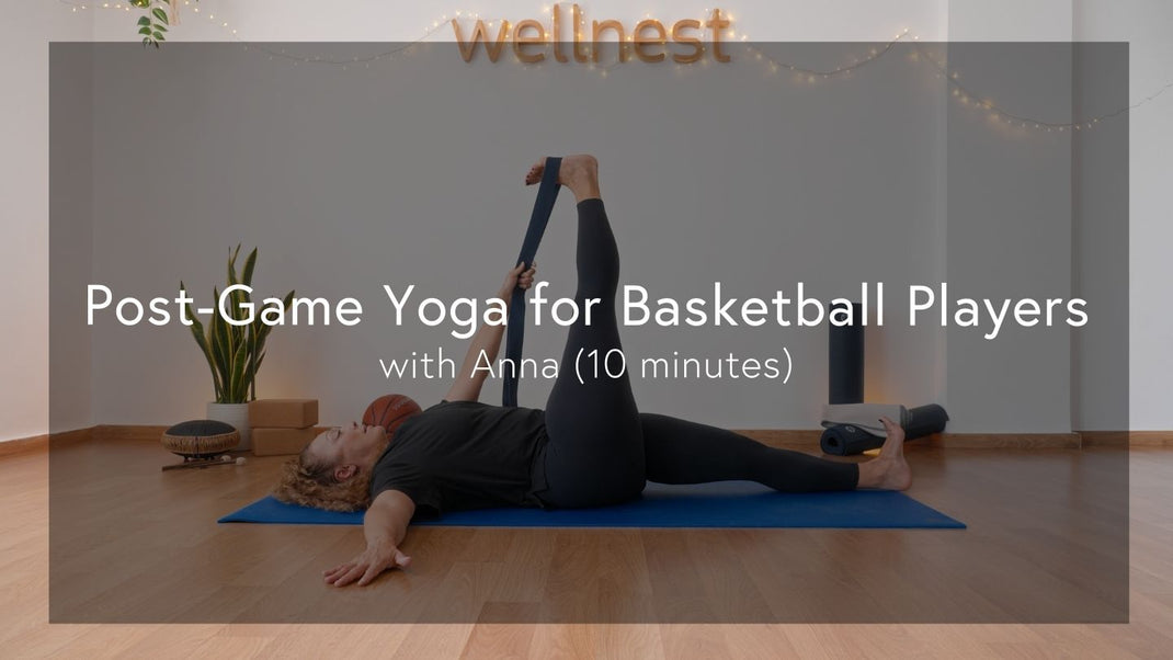 A person practices a leg stretch on a blue yoga mat in a cozy, well-lit room decorated with plants and warm lights.