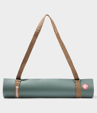 Tapis de yoga Manduka bleu sarcelle roulé, maintenu par un porte-tapis Commuter marron avec des sangles réglables et une bandoulière rembourrée pour faciliter le transport