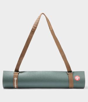 Tapis de yoga Manduka bleu sarcelle roulé, maintenu par un porte-tapis Commuter marron avec des sangles réglables et une bandoulière rembourrée pour faciliter le transport