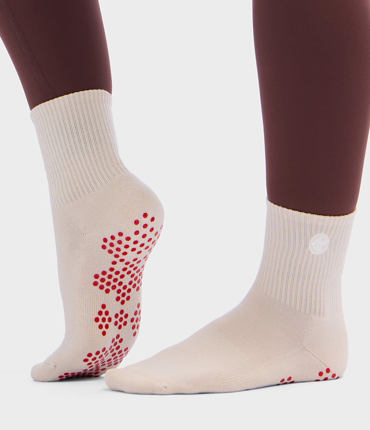 Chaussettes de Pilates mi-mollet couleur crème Manduka, avec des points antidérapants en silicone rouge sur les semelles et les talons pour plus de stabilité et un placement précis des pieds
