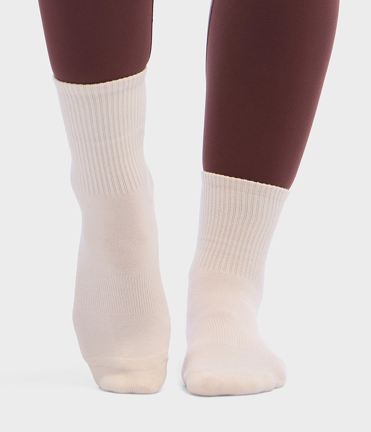 Chaussettes de Pilates blanches mi-montantes Manduka portées avec des leggings bordeaux, offrant une couverture côtelée à la cheville et un ajustement confortable