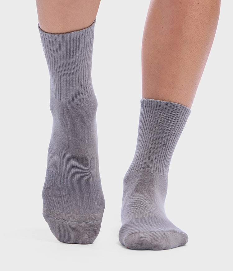 Chaussettes basses grises Manduka portées aux pieds, avec des bords-côtes à la cheville et un tissu en maille lisse sur fond clair