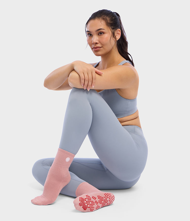 Femme portant des chaussettes antidérapantes de Pilates mi-montantes roses Manduka Equilibria, avec un motif antidérapant en silicone rouge visible sur la semelle