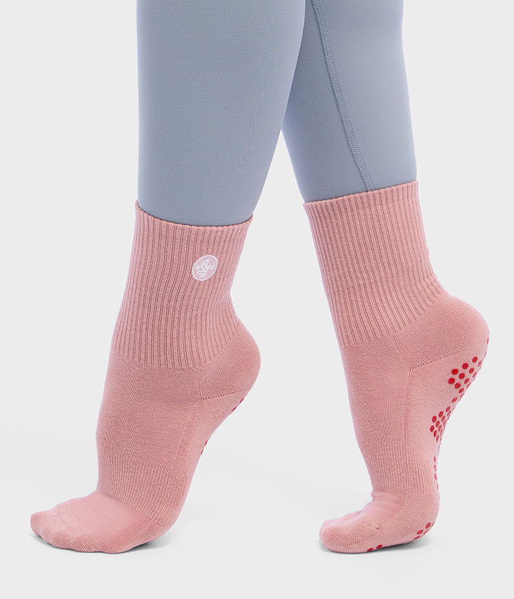 Chaussettes demi-montantes de Pilates roses Manduka Equilibria portées par un modèle, avec des picots antidérapants en silicone rouges sous le pied et des bords-côtes aux chevilles