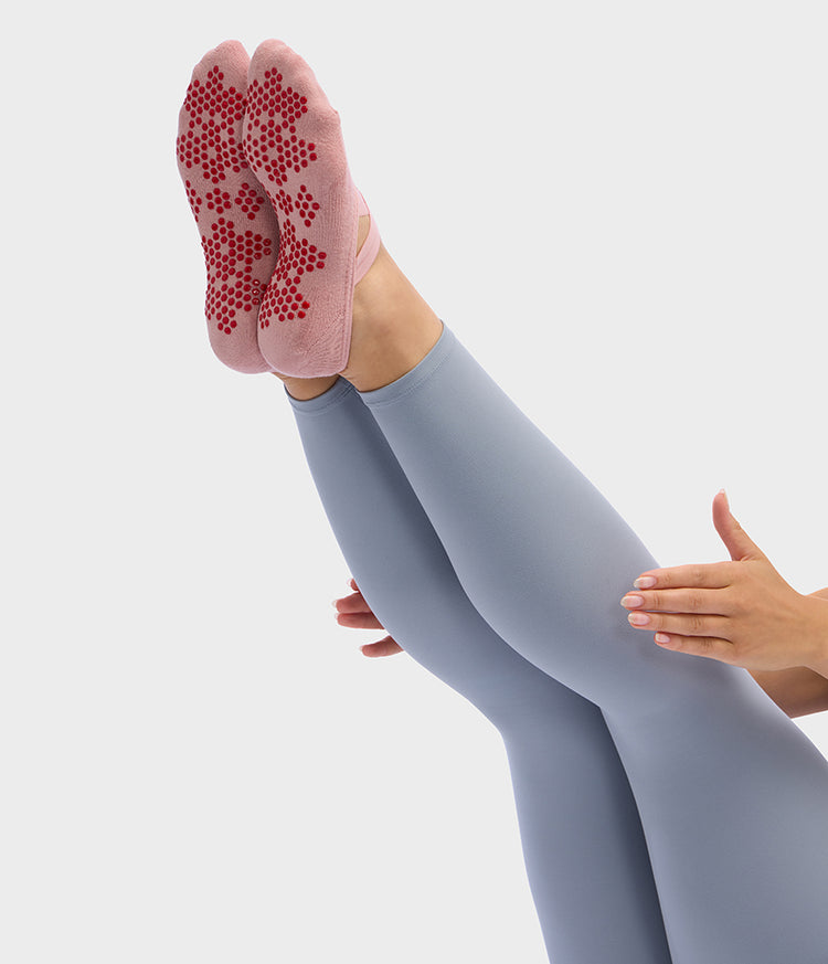 Manduka Equilibria Pilates slipper socks in pink with red silicone grip dots on raised feet during a Pilates exercise