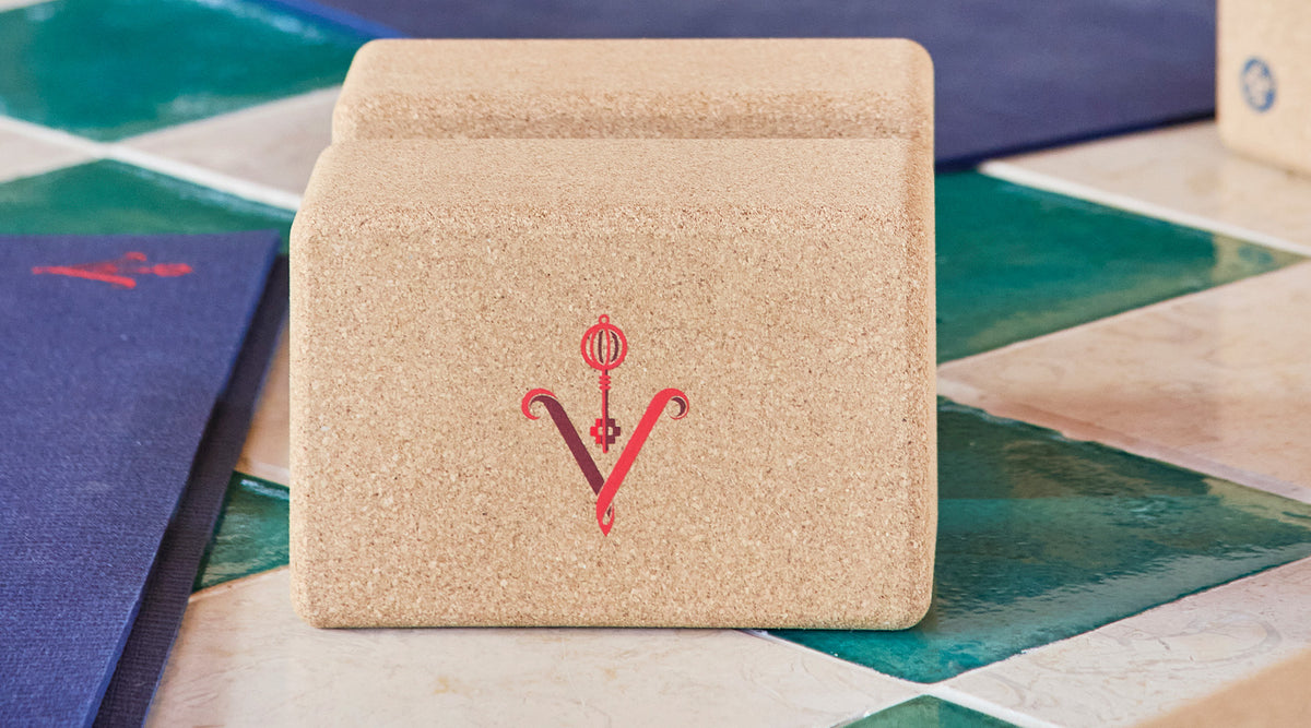 Two stacked Manduka cork yoga blocks with a red logo resting on a colorful geometric tiled surface