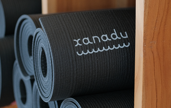 Rolled black Manduka yoga mats stacked beside a wooden surface, with the Manduka logo visible on the textured top mat.