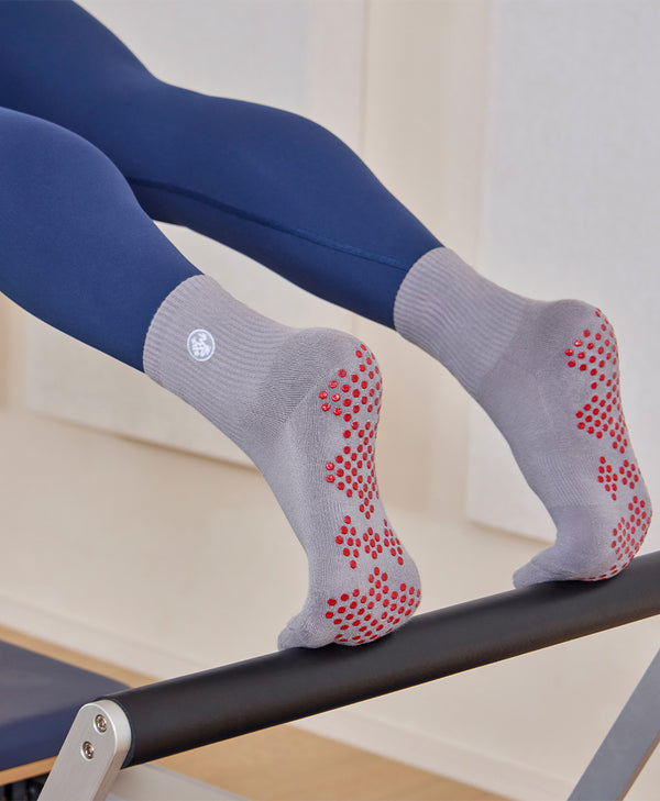 Person in navy leggings wearing gray grip socks with red dots while balancing on a black exercise barre.