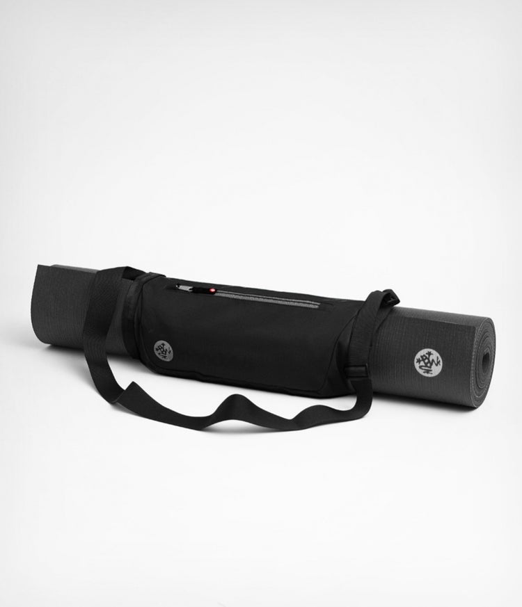 Manduka black yoga mat sling wrapped around a rolled yoga mat with a zippered storage pocket and adjustable shoulder strap