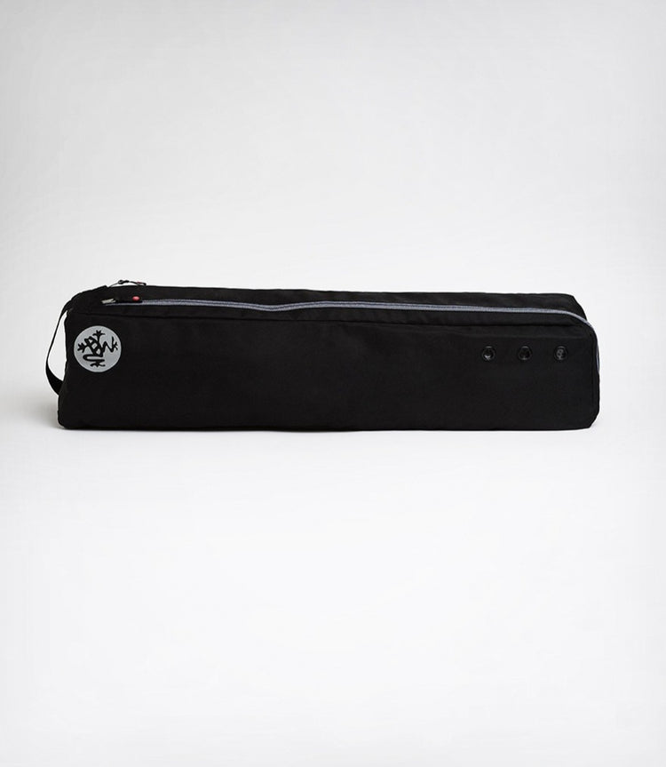 Black Manduka yoga mat carrier bag with a zippered top compartment and circular logo shown against a white background
